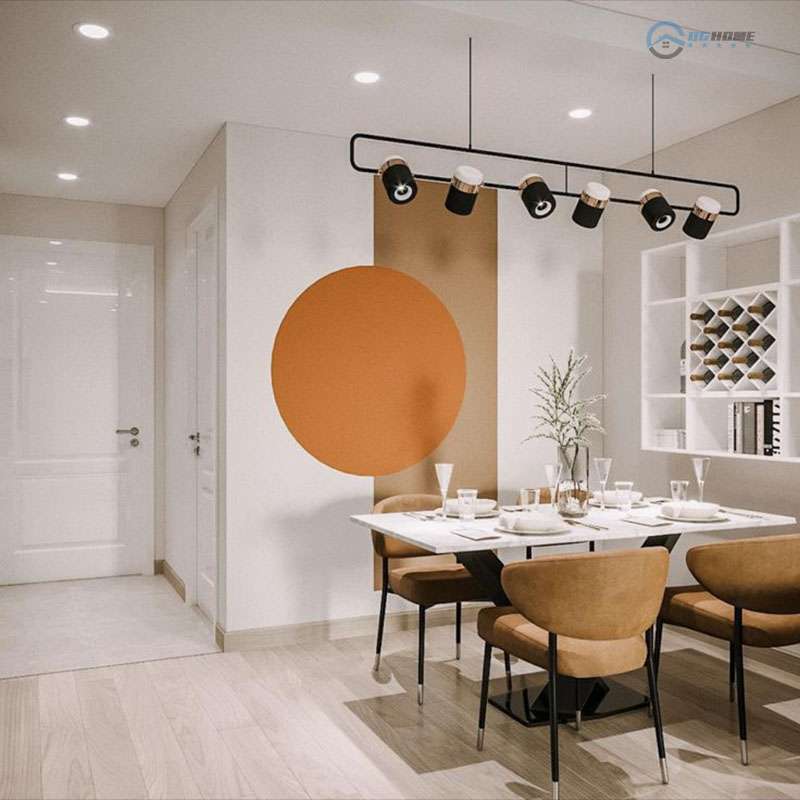 thiết kế nội thất chung cư 100m2 - Khu vực bàn ăn hiện đại với bàn mặt đá trắng, ghế bọc nệm màu nâu, điểm nhấn là mảng tường tròn màu cam đất nổi bật. Phía trên là đèn thả dạng thanh dài với chụp đèn tròn màu đen. Bên phải là kệ tường trắng với nhiều ngăn để rượu và sách.