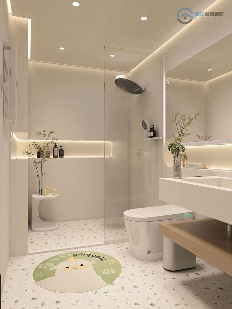 Một phòng tắm hiện đại với tông màu trắng chủ đạo, có vòi sen tắm đứng được ngăn cách bằng kính, bồn cầu thông minh, bồn rửa mặt màu trắng với kệ gỗ bên dưới, và sàn gạch terrazzo. Ánh sáng âm trần và đèn LED hắt tạo không gian sáng sủa và ấm cúng.